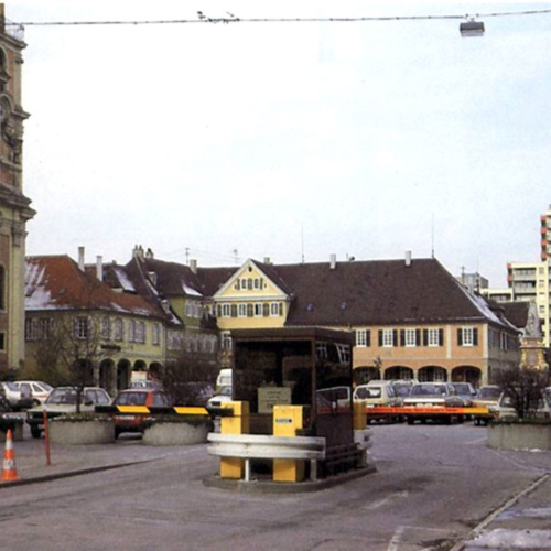 Das Foto zeigt den Markplatz in der Innenstadt in seinem früheren Zustand. Ein Parkplatz befindet sich auf dem Platz.